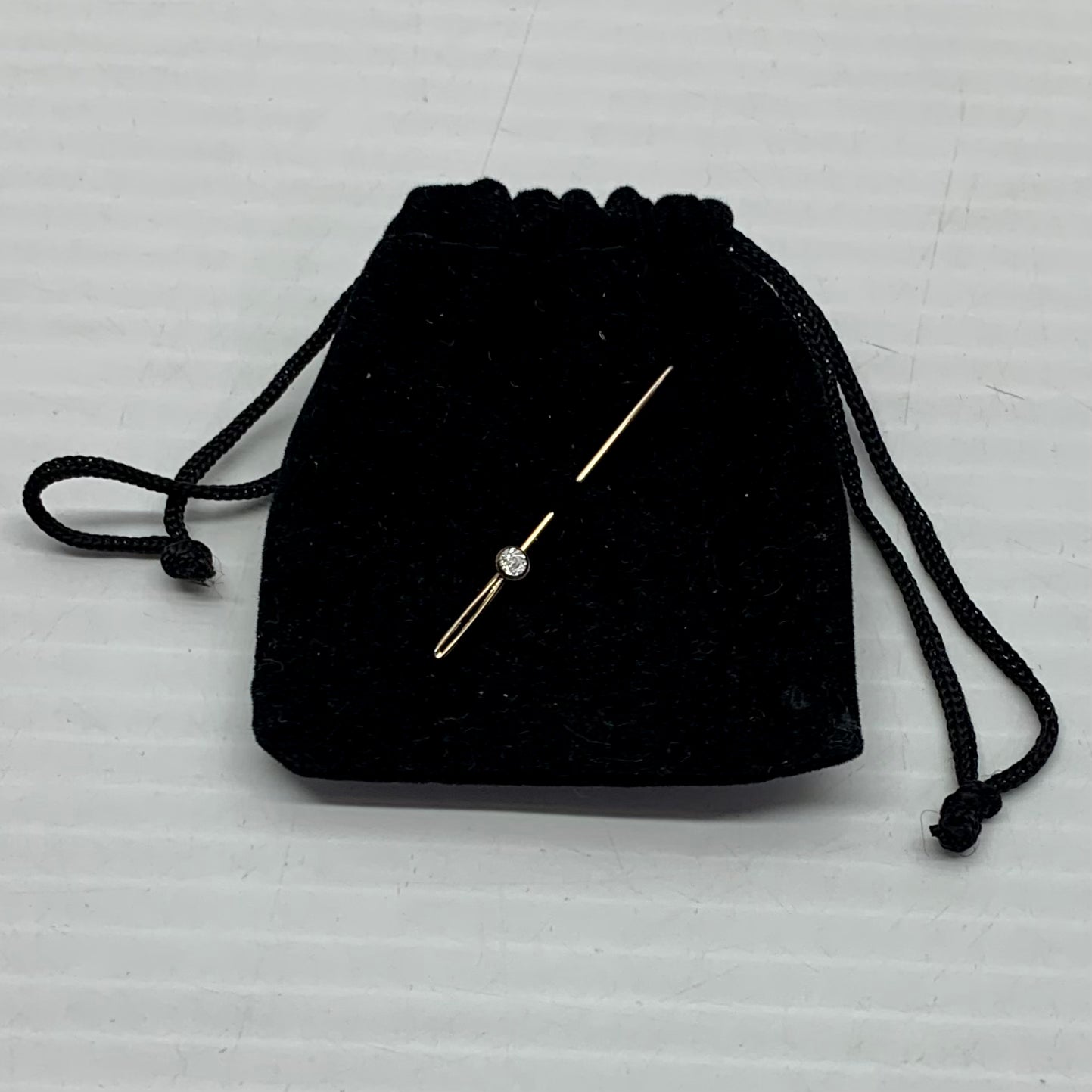 A vintage brooch pin with a genuine diamond centerpiece, attached to a black fabric bag.