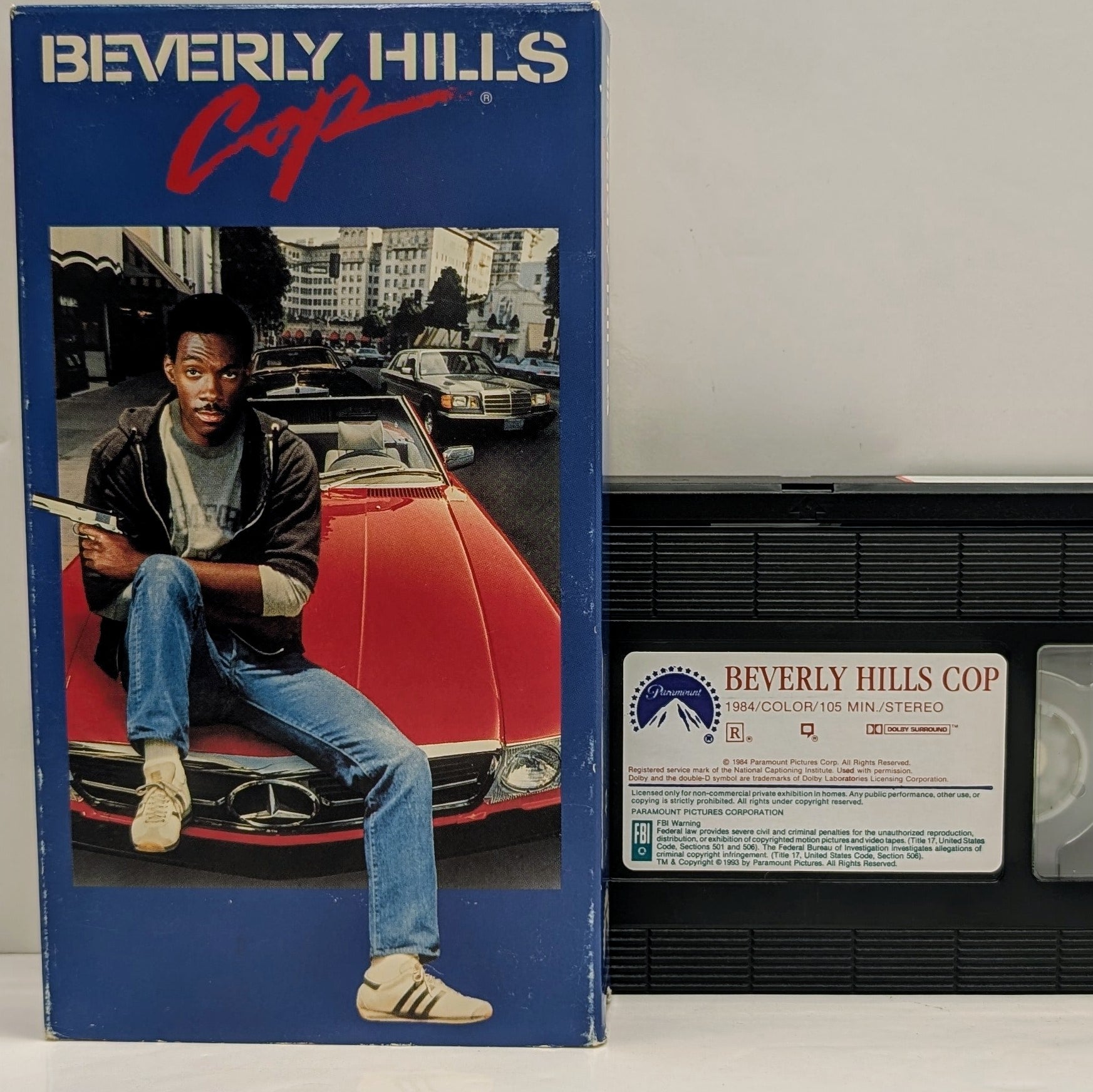 VHS tape and box cover for the movie Beverly Hills Cop, featuring an image of the main character with a red sports car in the background.