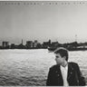 Album cover with a person by a waterfront with a city skyline in the background