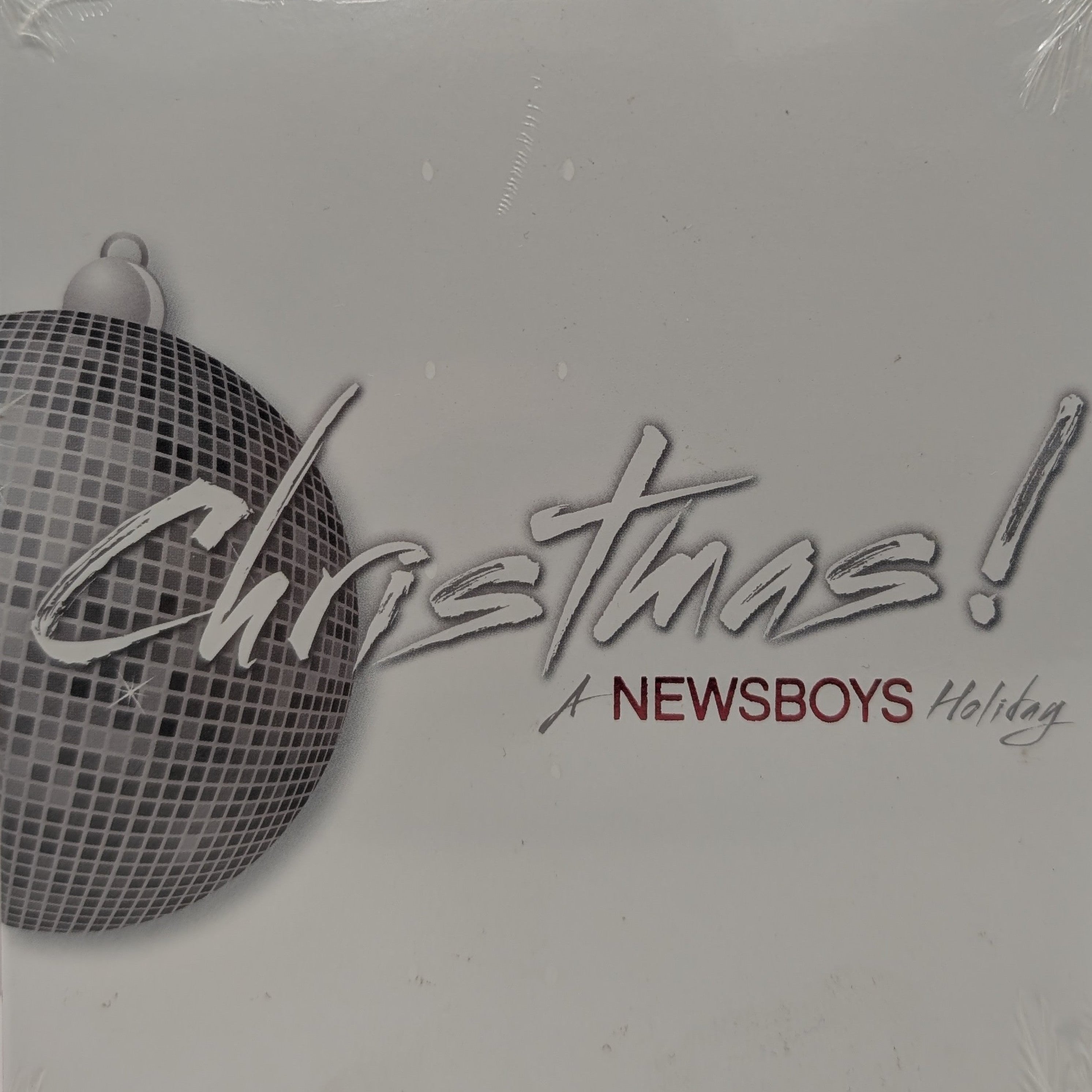 A square album cover for 'Christmas! A Newsboys Holiday' wrapped in clear plastic. The design features a silver disco ball ornament on the left and the text 'Christmas!' in large silver script, with 'A NEWSBOYS Holiday' written below in silver and dark red.
