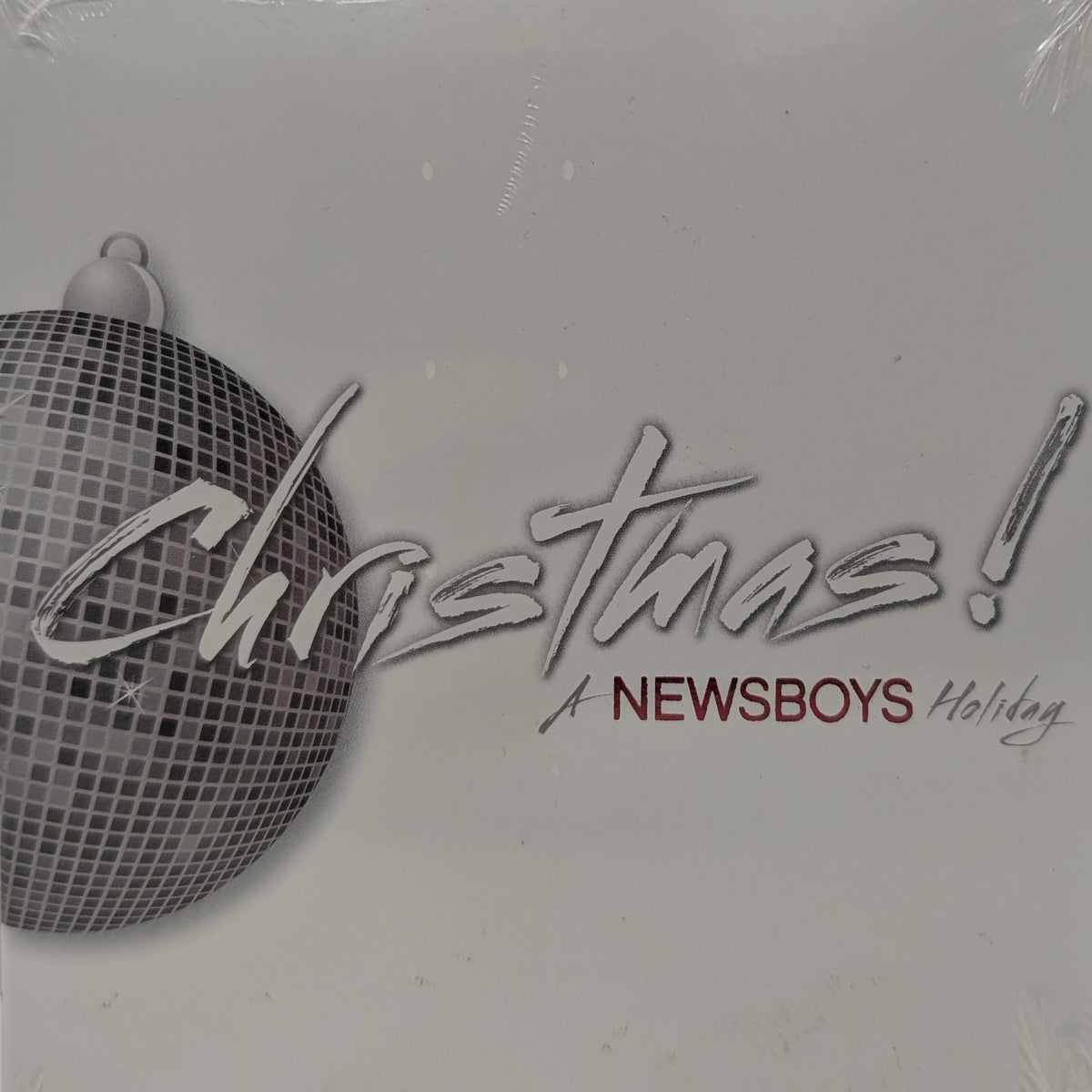 A square album cover for 'Christmas! A Newsboys Holiday' wrapped in clear plastic. The design features a silver disco ball ornament on the left and the text 'Christmas!' in large silver script, with 'A NEWSBOYS Holiday' written below in silver and dark red.