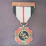 A military-style medal pendant with a circular gold-toned top medallion featuring red, orange, and black enamel, suspended from a ribbon with black, white, and red sections, and a bronze-toned bar at the bottom reading 'ELO'S GREATEST HITS'.