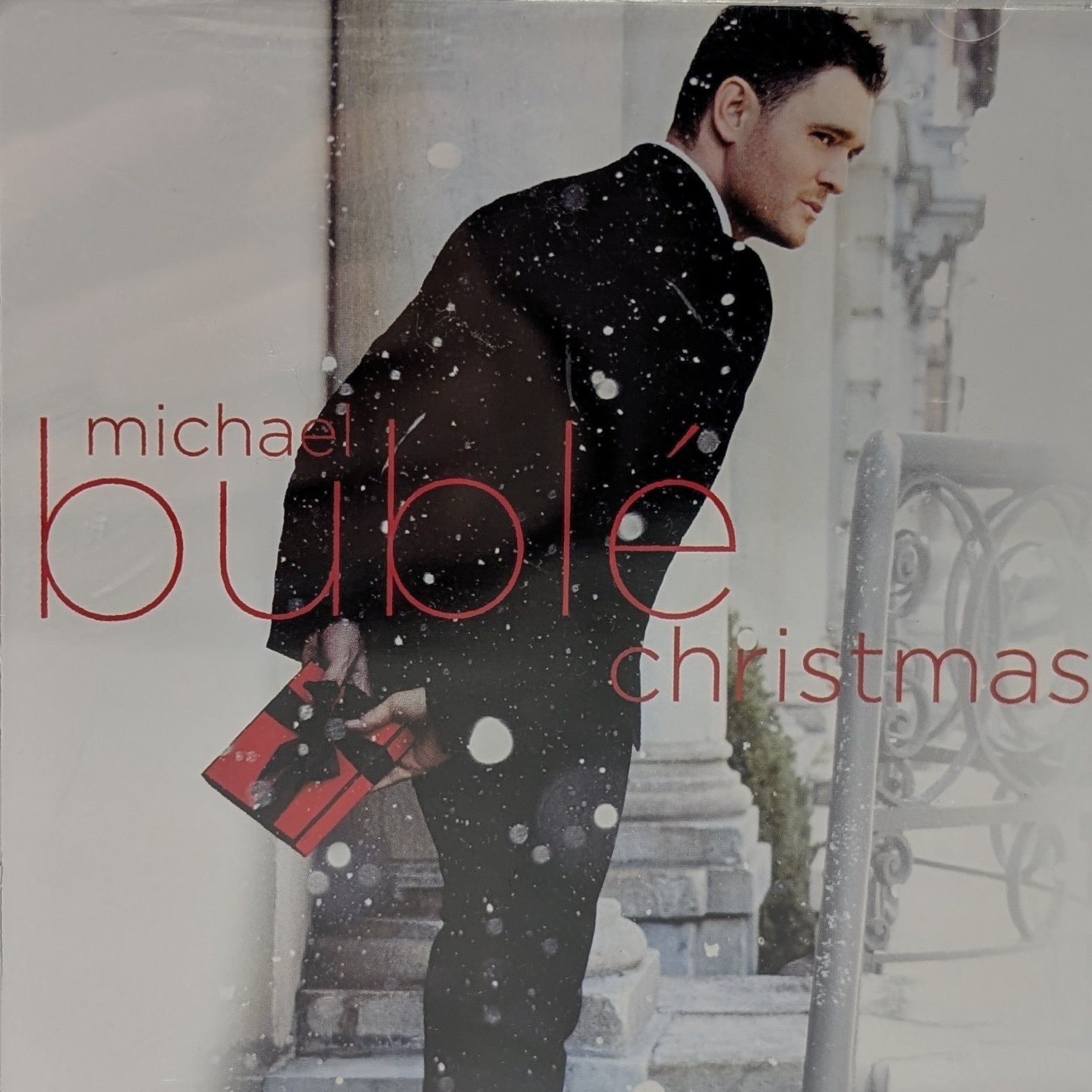 Michael Bublé's Christmas album cover on CD, featuring a man in a black suit standing in snow with a red gift bag, with the text 'michael bublé christmas' in red.