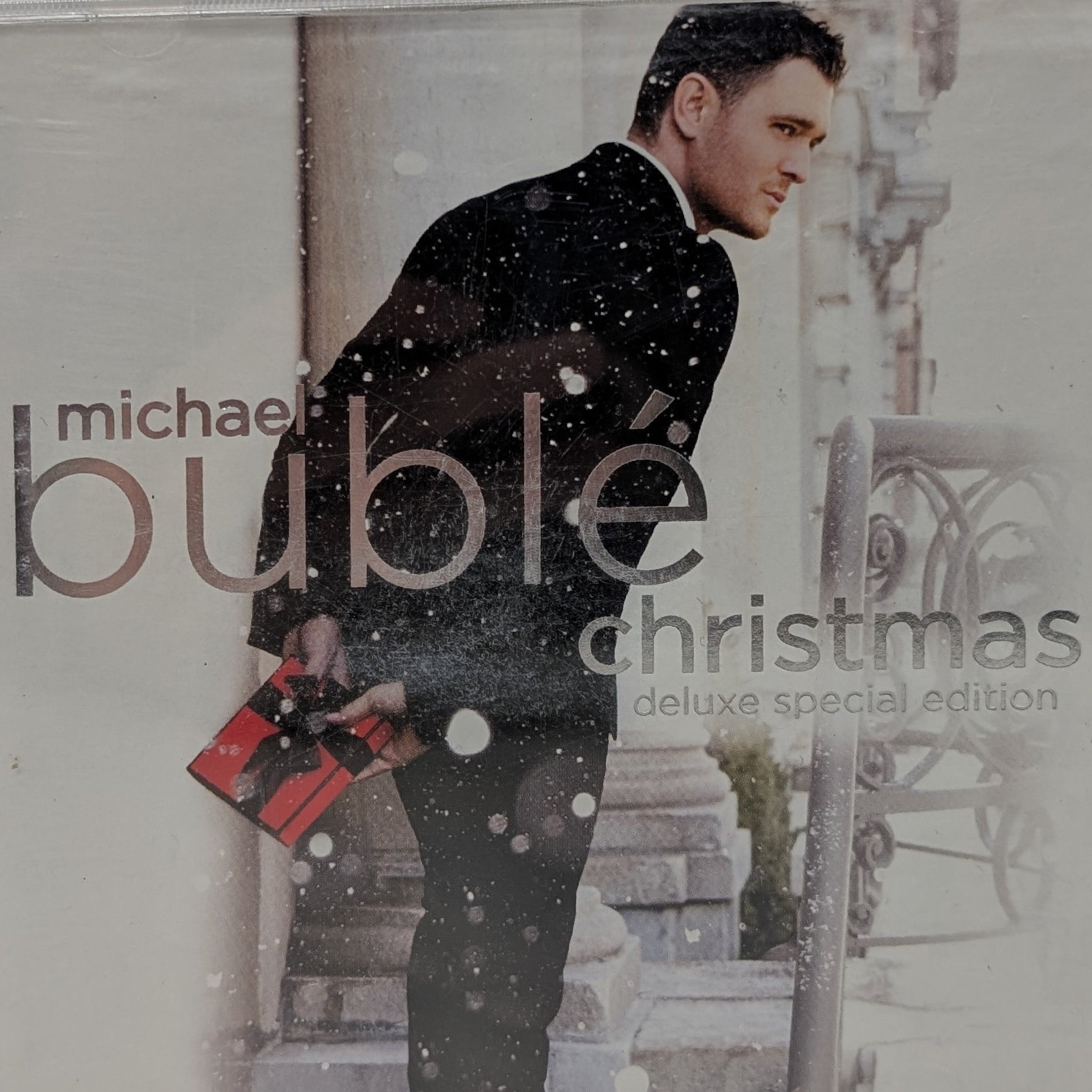 Michael Bublé 'Christmas Deluxe Special Edition' CD album cover in a clear jewel case, featuring a man in a black suit holding a red gift box against a snowy outdoor background.