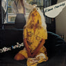 Album cover for Kim Carnes' 'Mishapen Identity', featuring a blonde woman sitting on a dark couch in a yellow floral dress, with a blurred figure in the background.