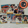 Collection of Philadelphia Flyers hockey trading cards on a white surface with the Flyers logo.
