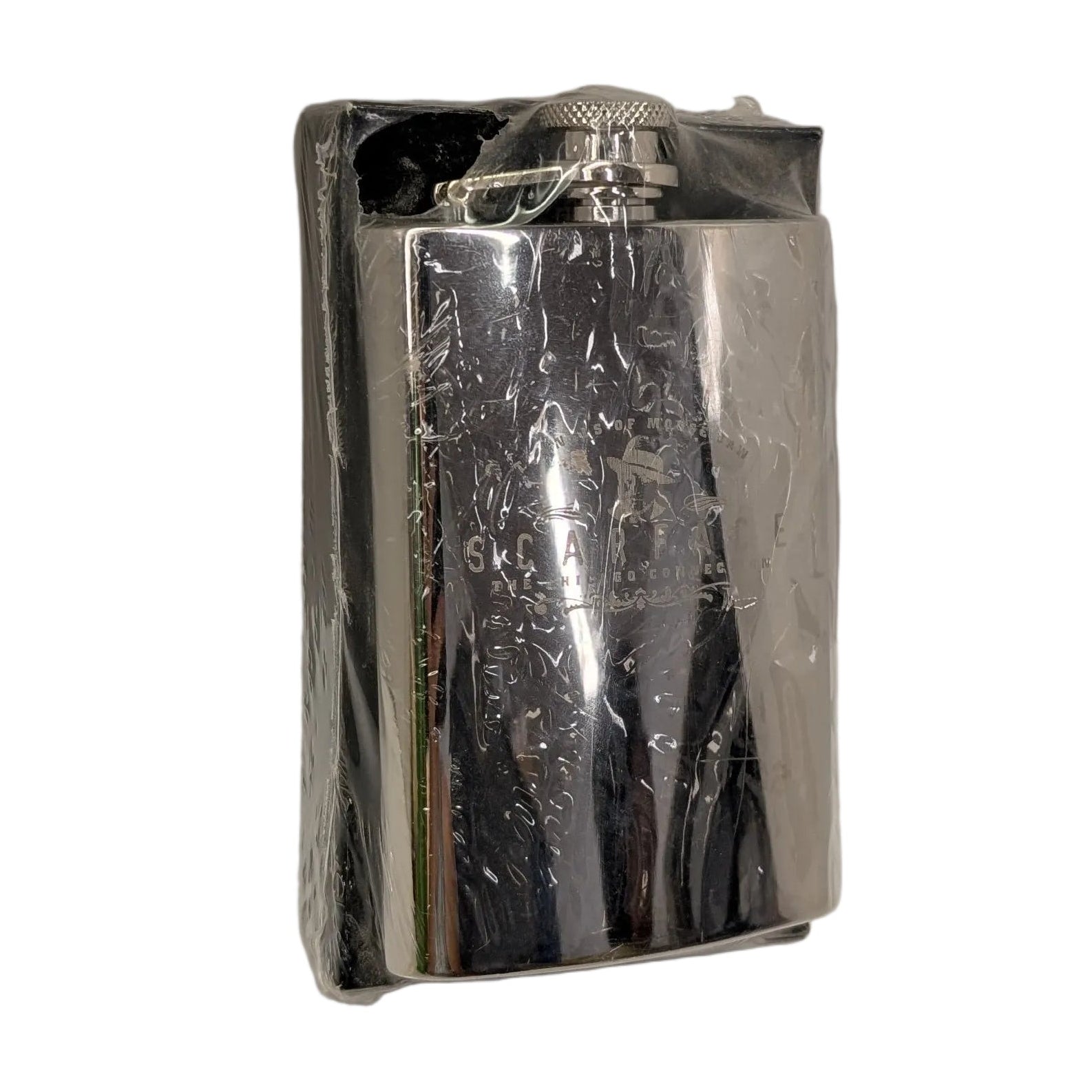 A small rectangular metallic silver object wrapped in clear plastic, standing upright in the corner of a white studio setup.