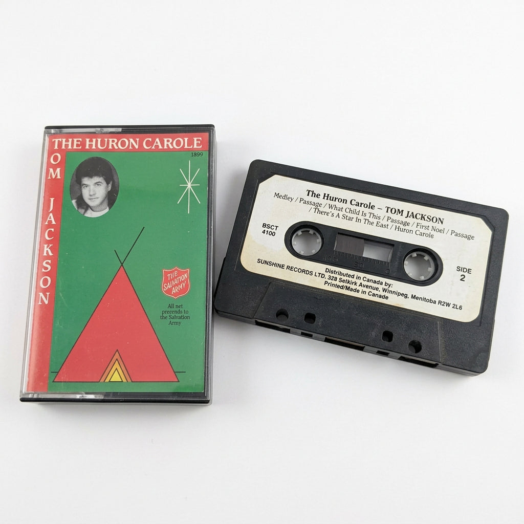 A vintage cassette tape and its paper sleeve for 'The Huron Carol' by Tom Jackson, placed on a white surface.