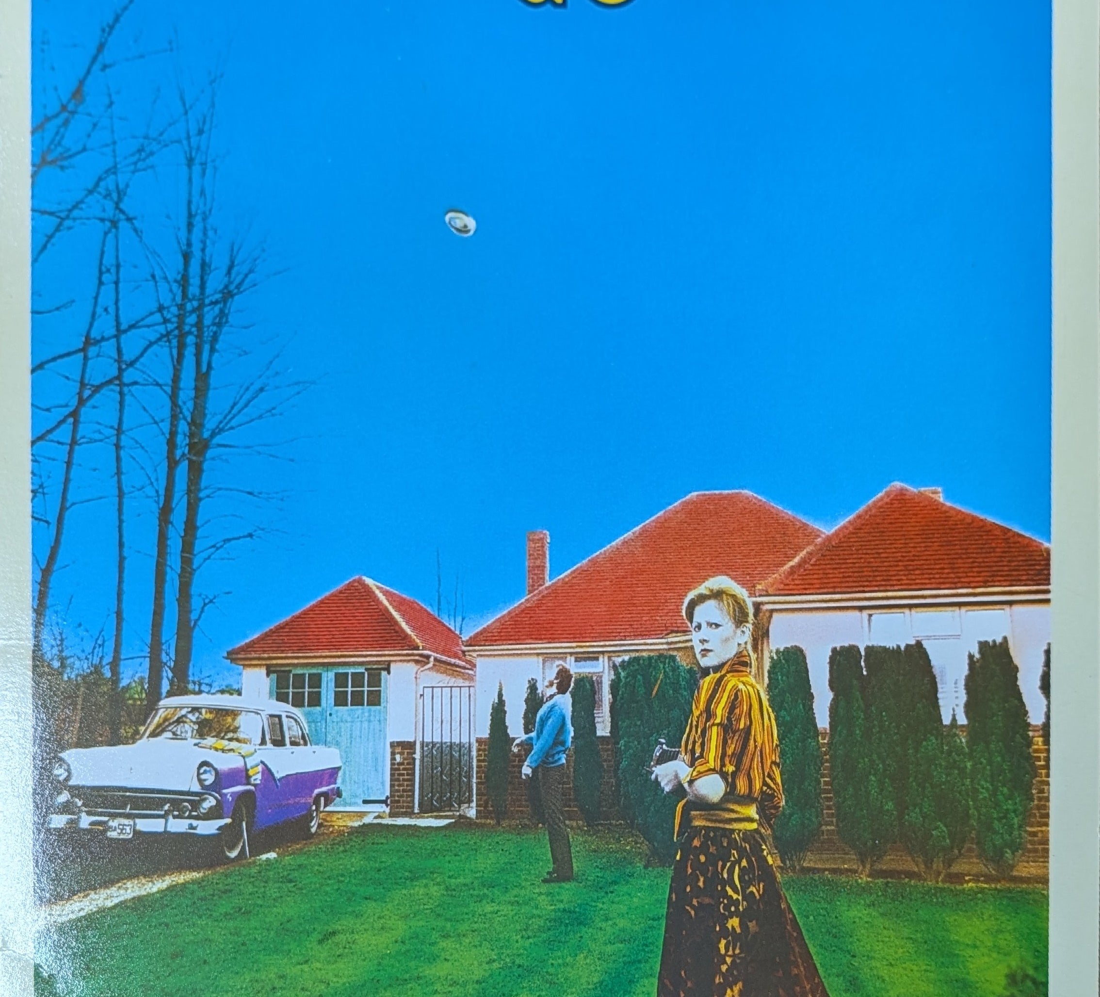 Album cover with a woman, car, and houses under a blue sky.