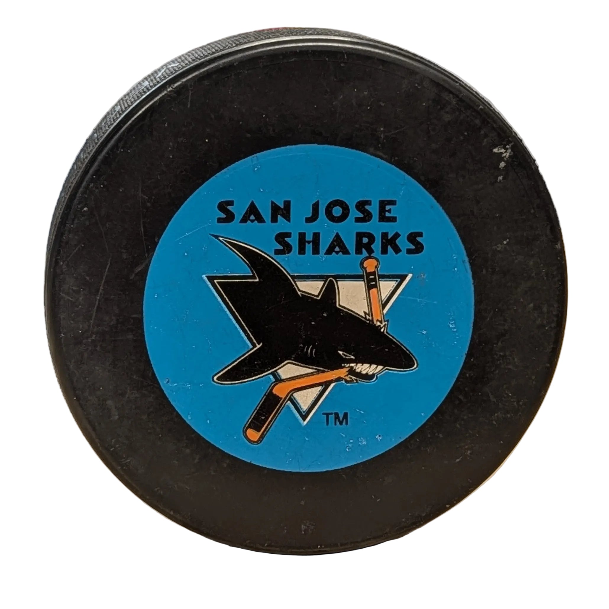 A black hockey puck featuring a San Jose Sharks logo on the top with a white background.