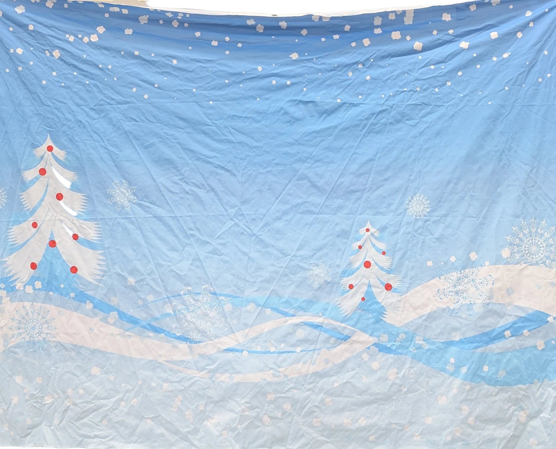 A light blue fabric wall tapestry featuring a winter Christmas scene with two decorated trees, snow, and falling snowflakes, displayed against a white background.